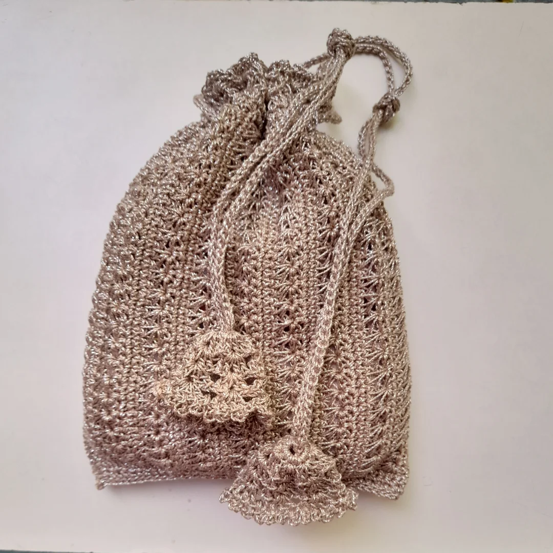 A beige drawstring potli bag in open mesh work with tasselled ties.