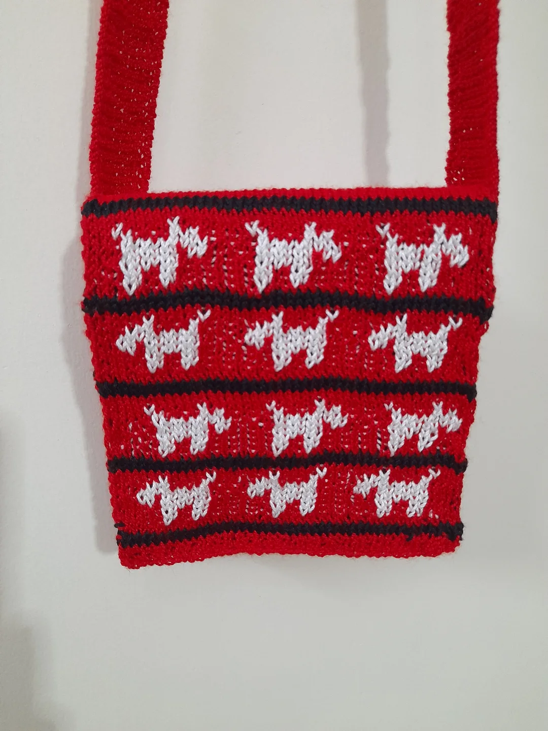 A red sling bag with a repeating white dog motif worked into the fabric.